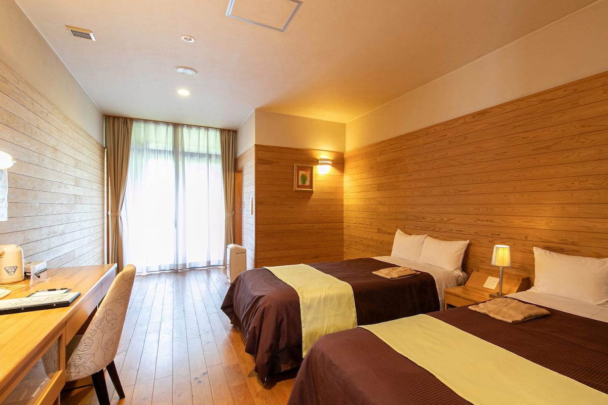Habitación de hotel con dos camas, un escritorio, una silla y una ventana con cortinas.