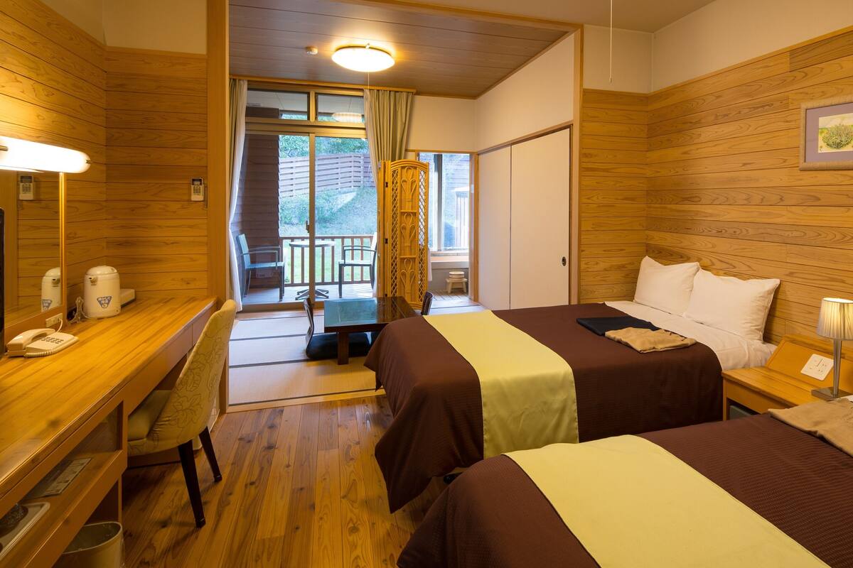 Habitación de hotel con dos camas, un escritorio con teléfono, una silla y un balcón con vistas.