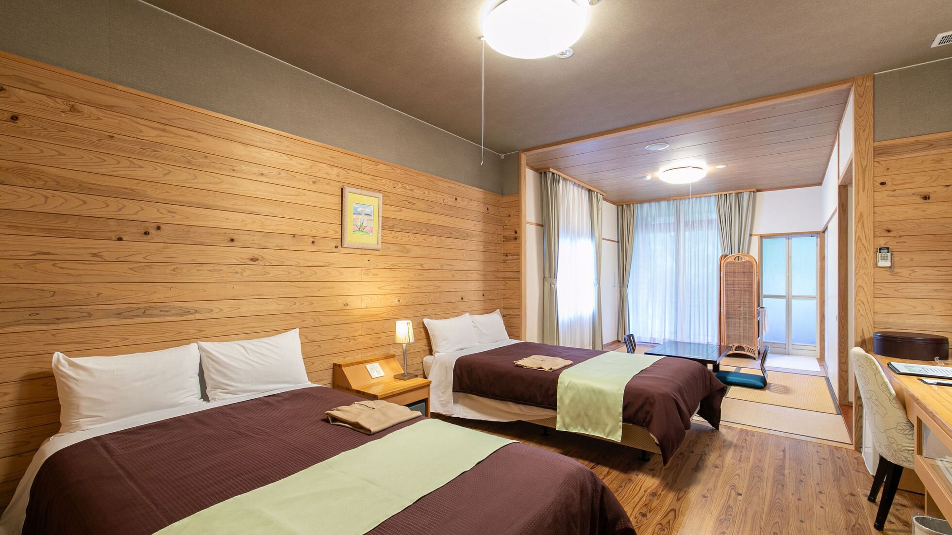 Ein Hotelzimmer mit zwei Betten, Holzwänden, einem Schreibtisch und Blick ins Freie.