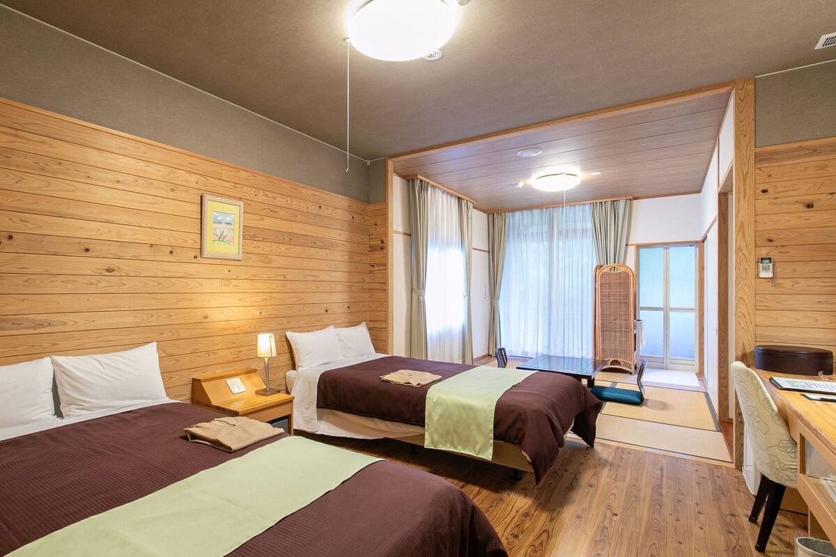 Habitación de hotel con dos camas, paredes de madera, un escritorio y vistas al exterior.