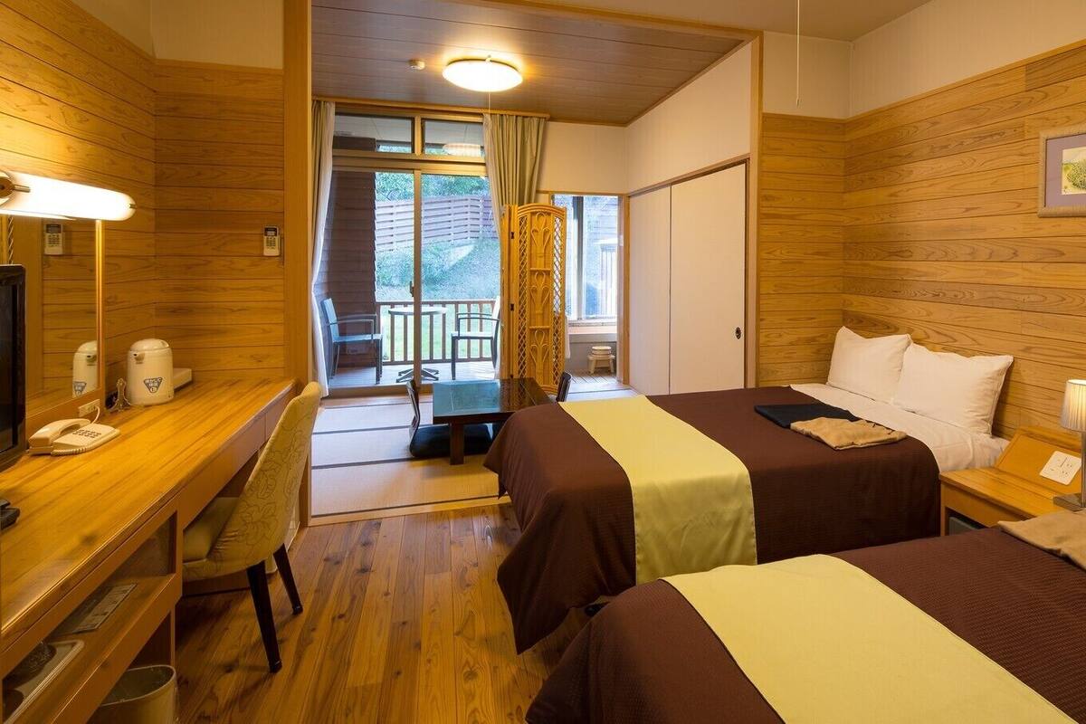 Habitación de hotel con dos camas, un escritorio con teléfono, una silla y un balcón con vistas.