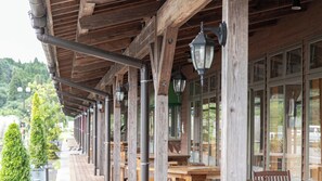 Un espace extérieur abrité, doté de poutres en bois et de poteaux en métal, et aménagé avec des tables et des chaises.