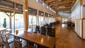 A spacious dining area with wooden tables and chairs, large windows, and a high ceiling with exposed beams. - Fontana No Oka Kamo (Aira)