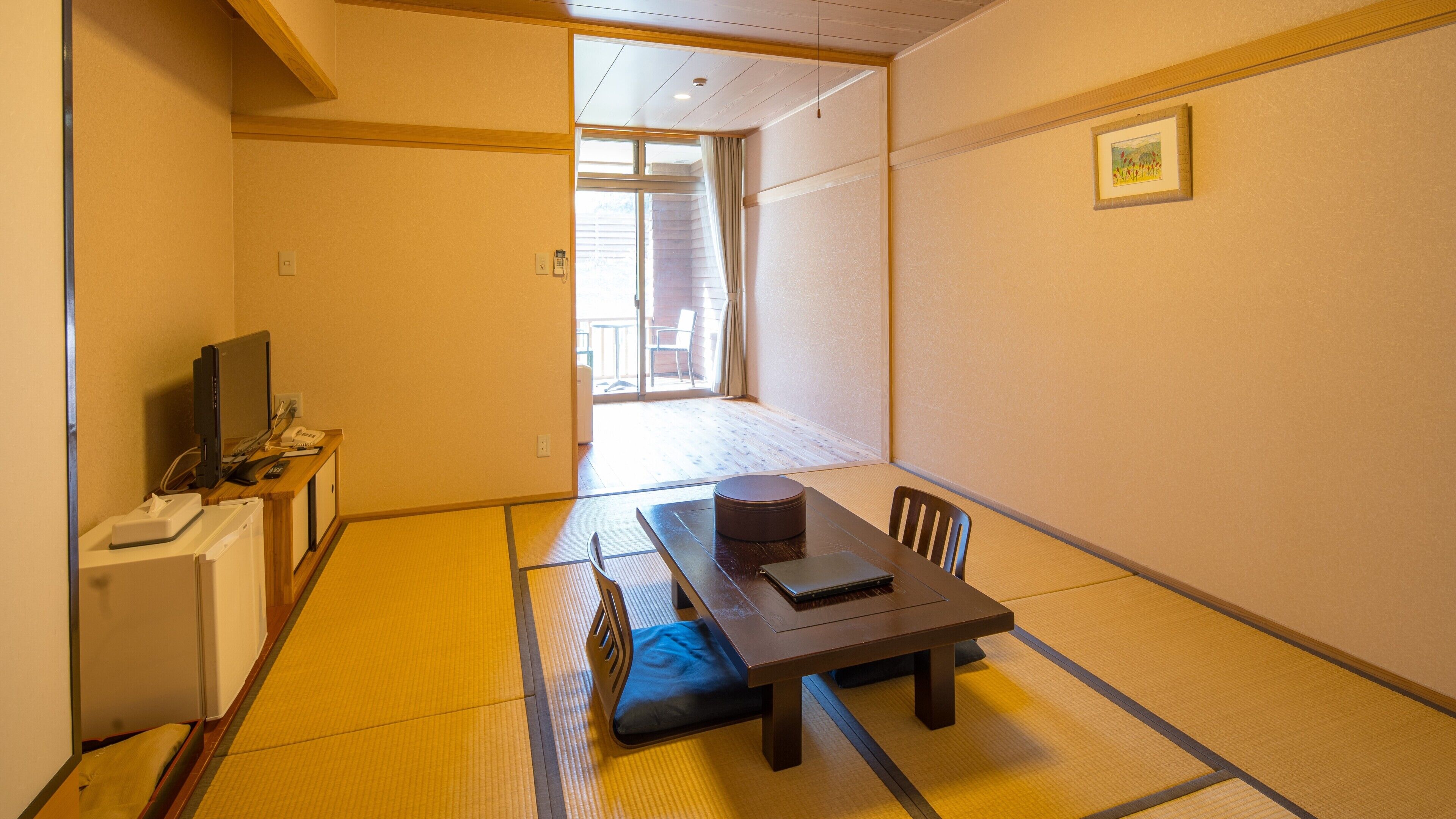 A traditional Japanese room with tatami flooring, a low table with a cushion, a television, and a small desk with a telephone.