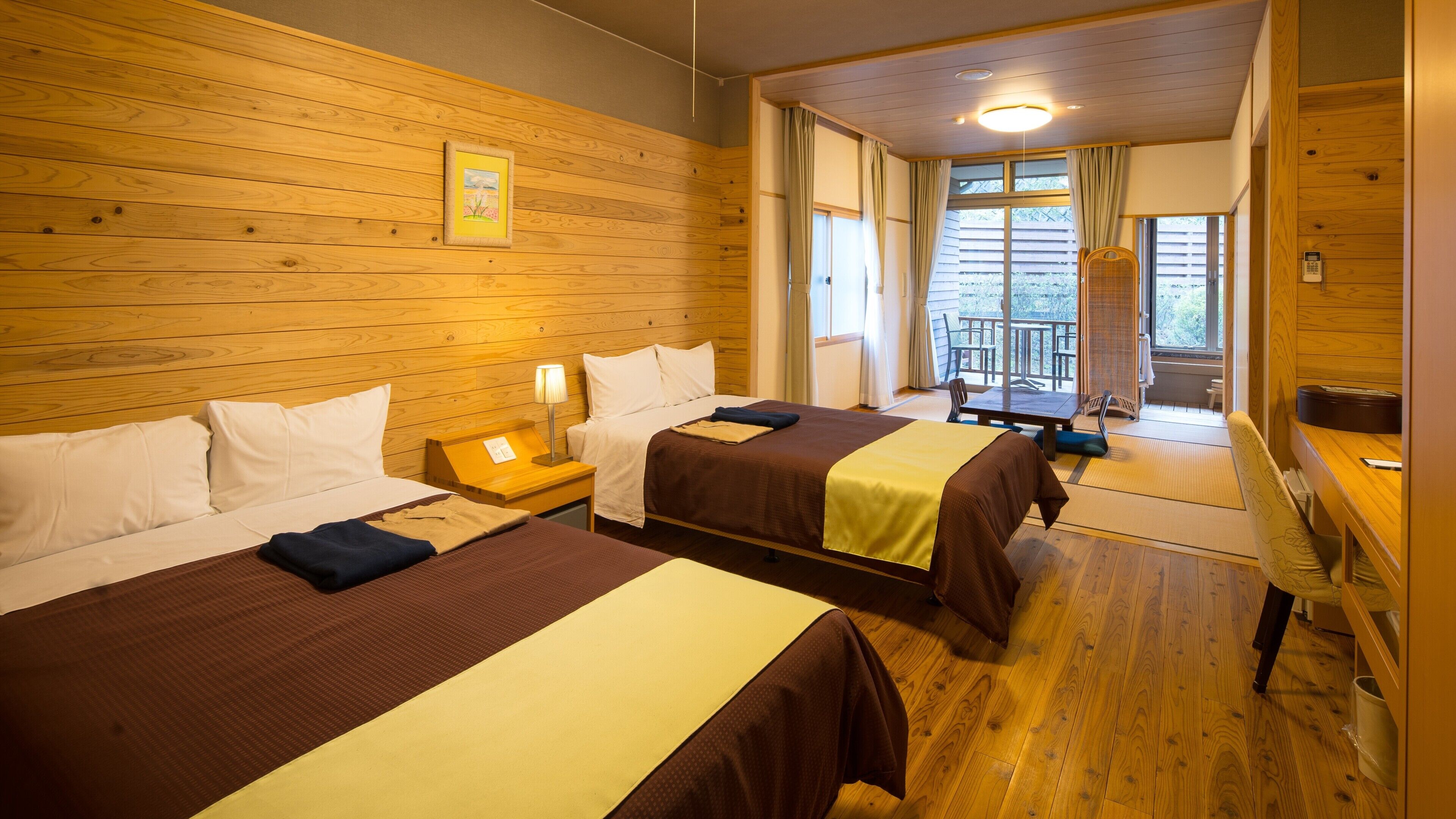 A hotel room with two beds, wooden walls, a small table, and a balcony with a view.