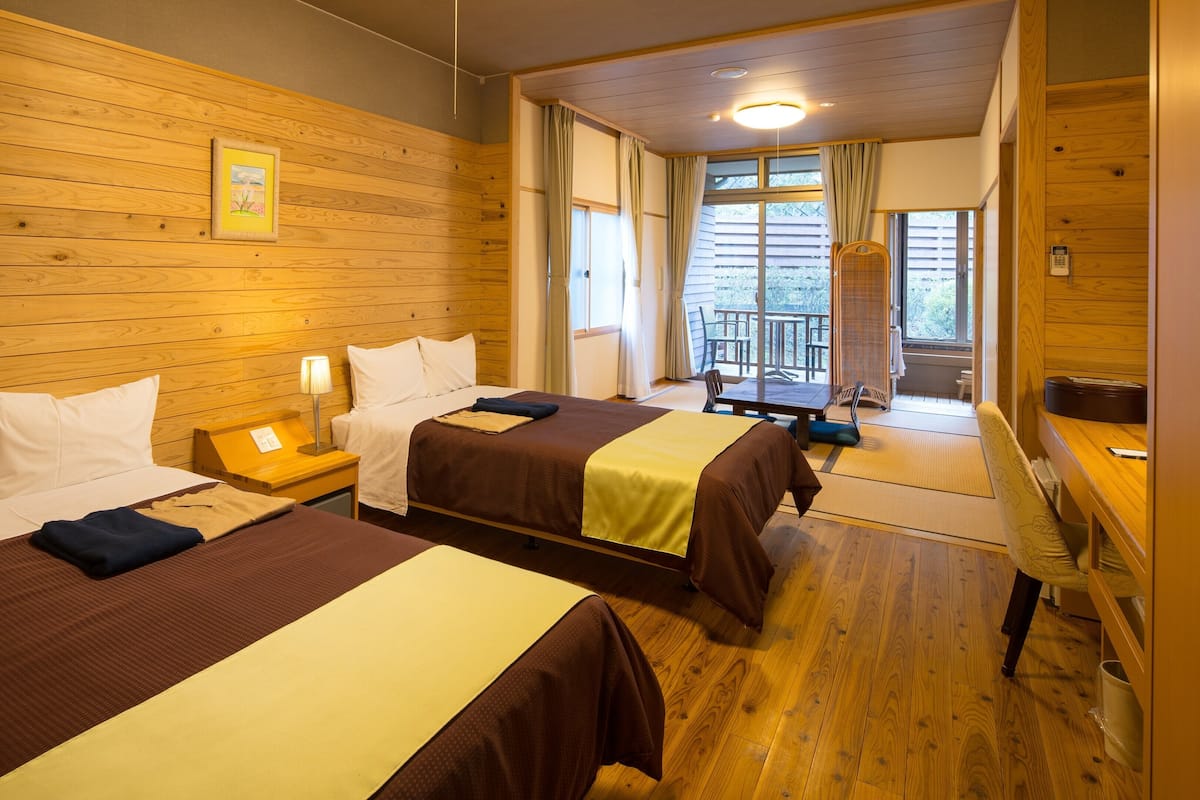 Habitación de hotel con dos camas, paredes de madera, una mesita y un balcón con vistas.
