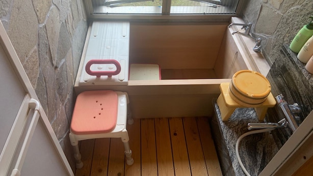 A small bathroom with a wooden floor, a white sink, a mirror, a window, and a red seat.