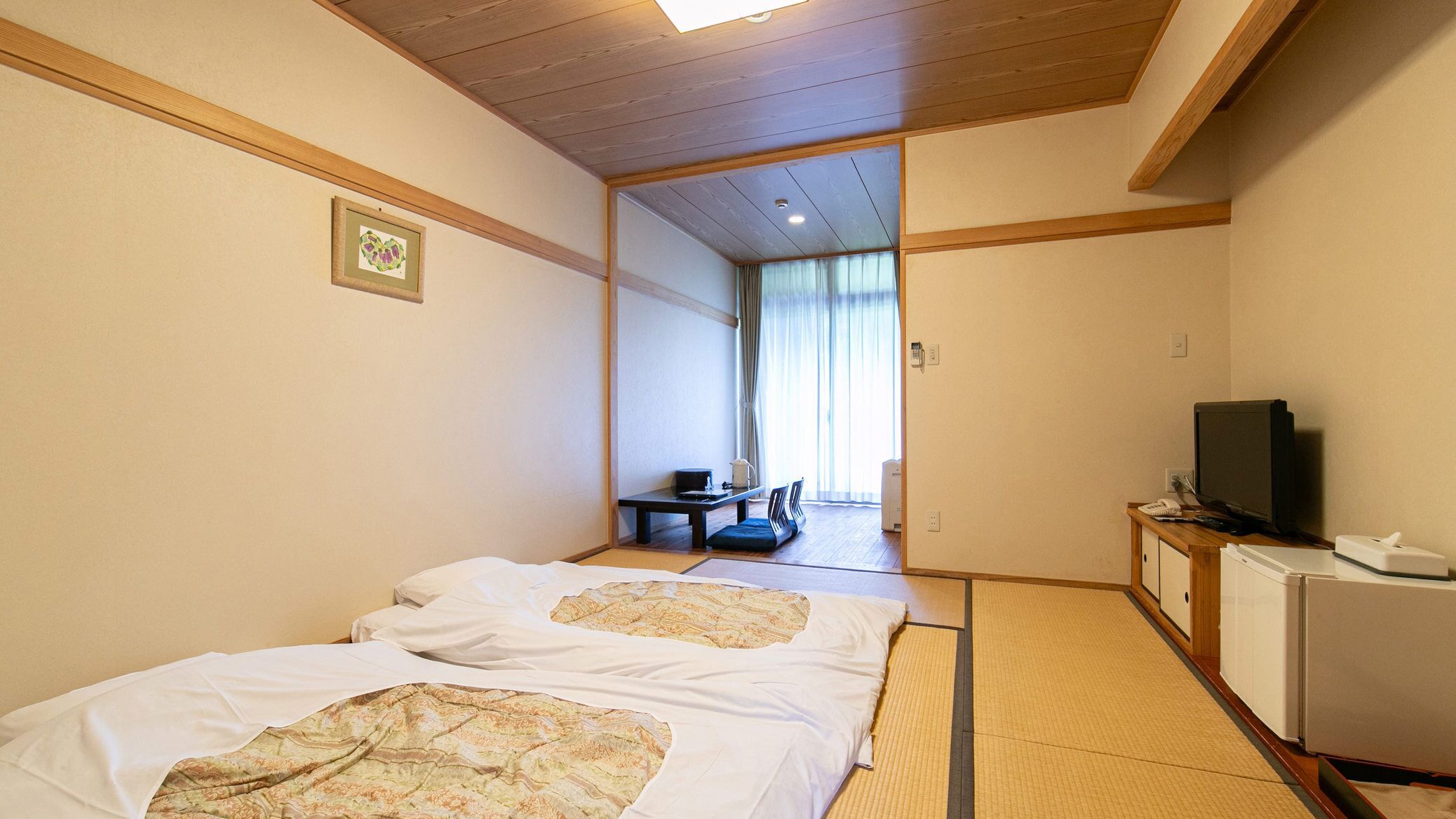 A hotel room with two beds, a desk, a television, and a small refrigerator.