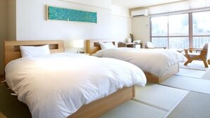 Habitación de hotel con dos camas, un ventanal grande y vistas de la ciudad.
