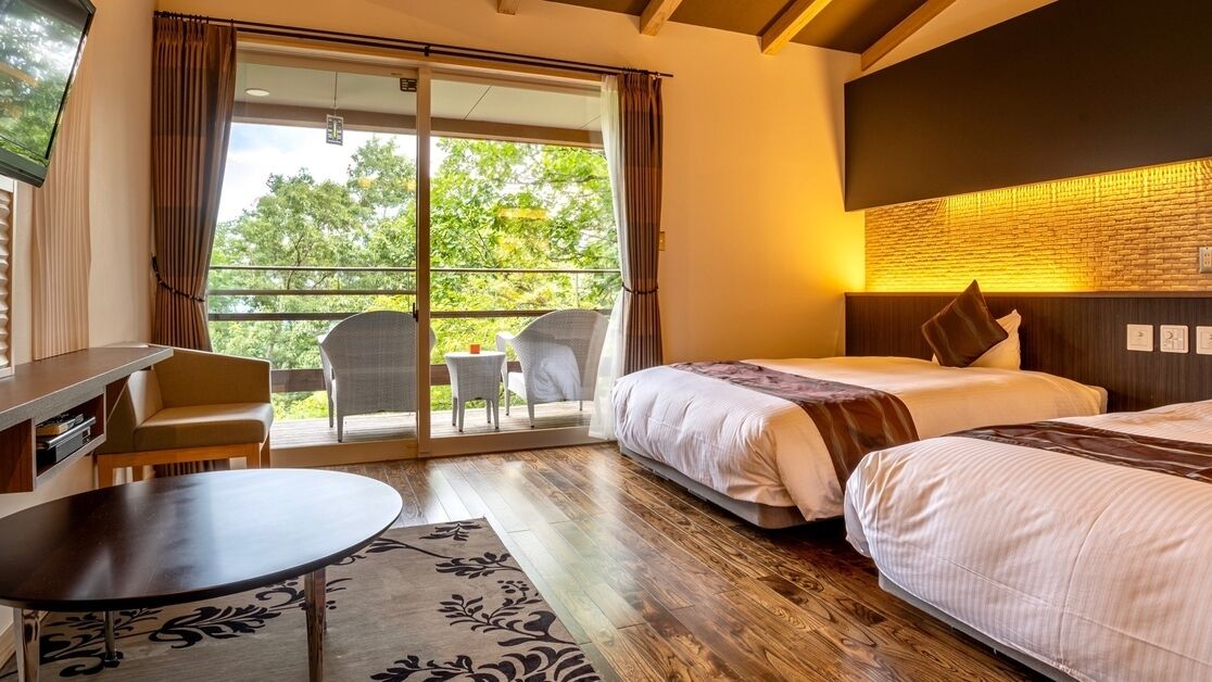 Habitación de hotel con cama, escritorio, silla, una mesita y balcón con vistas a árboles.