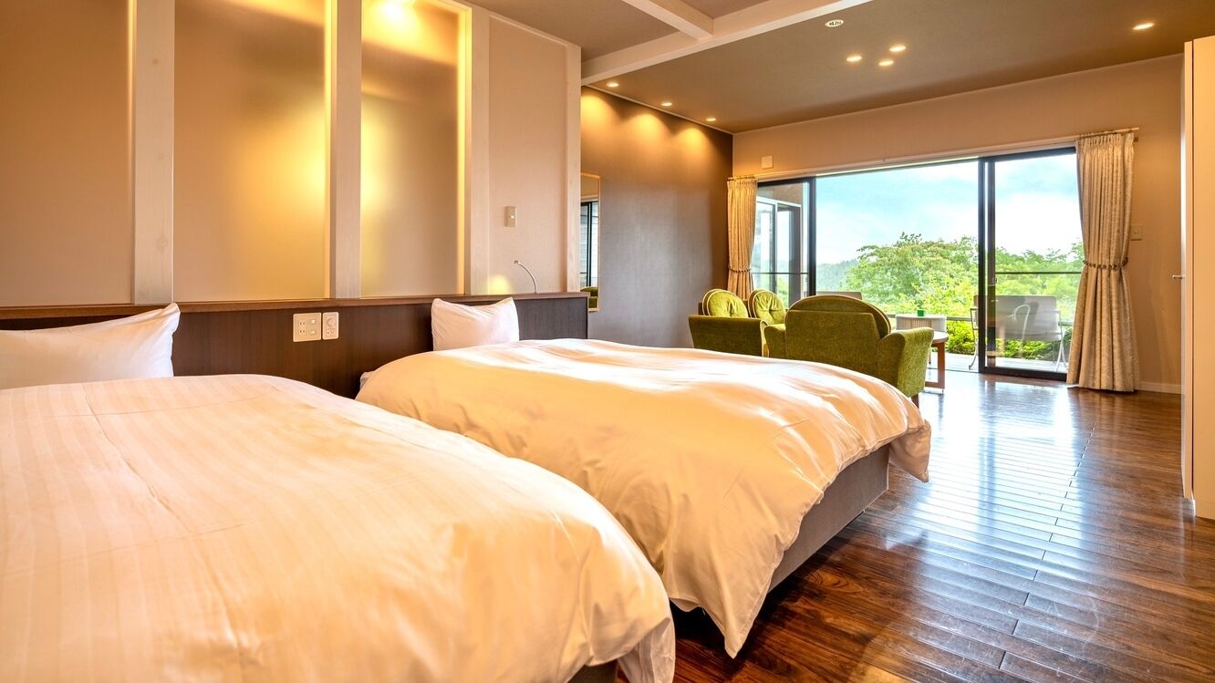 Ein Hotelzimmer mit zwei Betten, einem Balkon mit Tisch und Stühlen sowie einem großen Fenster.
