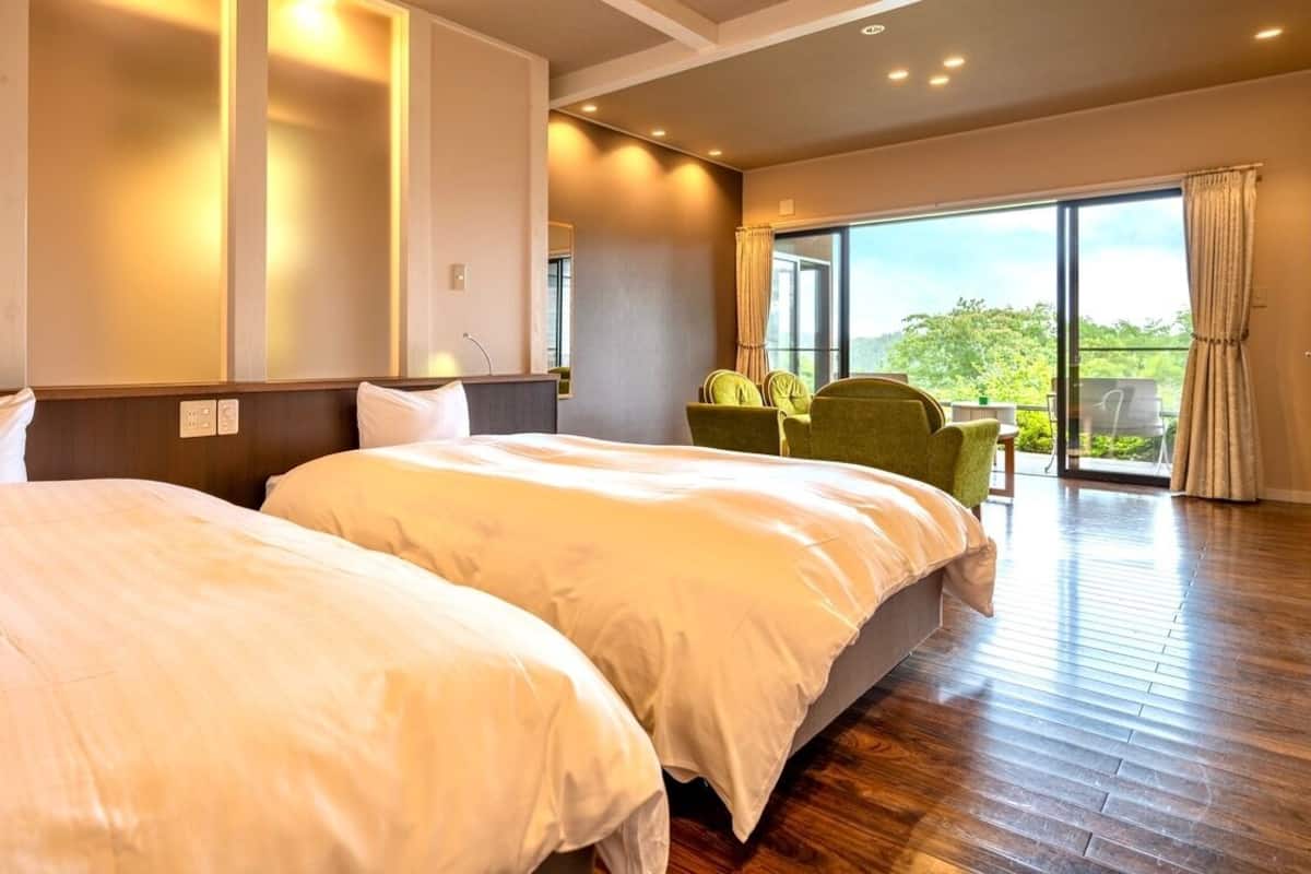 Ein Hotelzimmer mit zwei Betten, einem Balkon mit Tisch und Stühlen sowie einem großen Fenster.