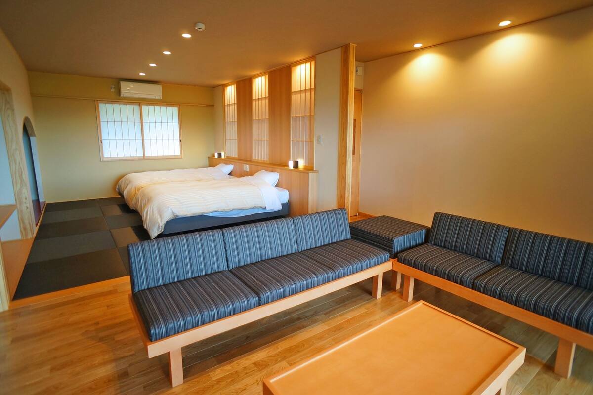 A hotel room with a bed, two sofas, a small table, and a window with blinds.