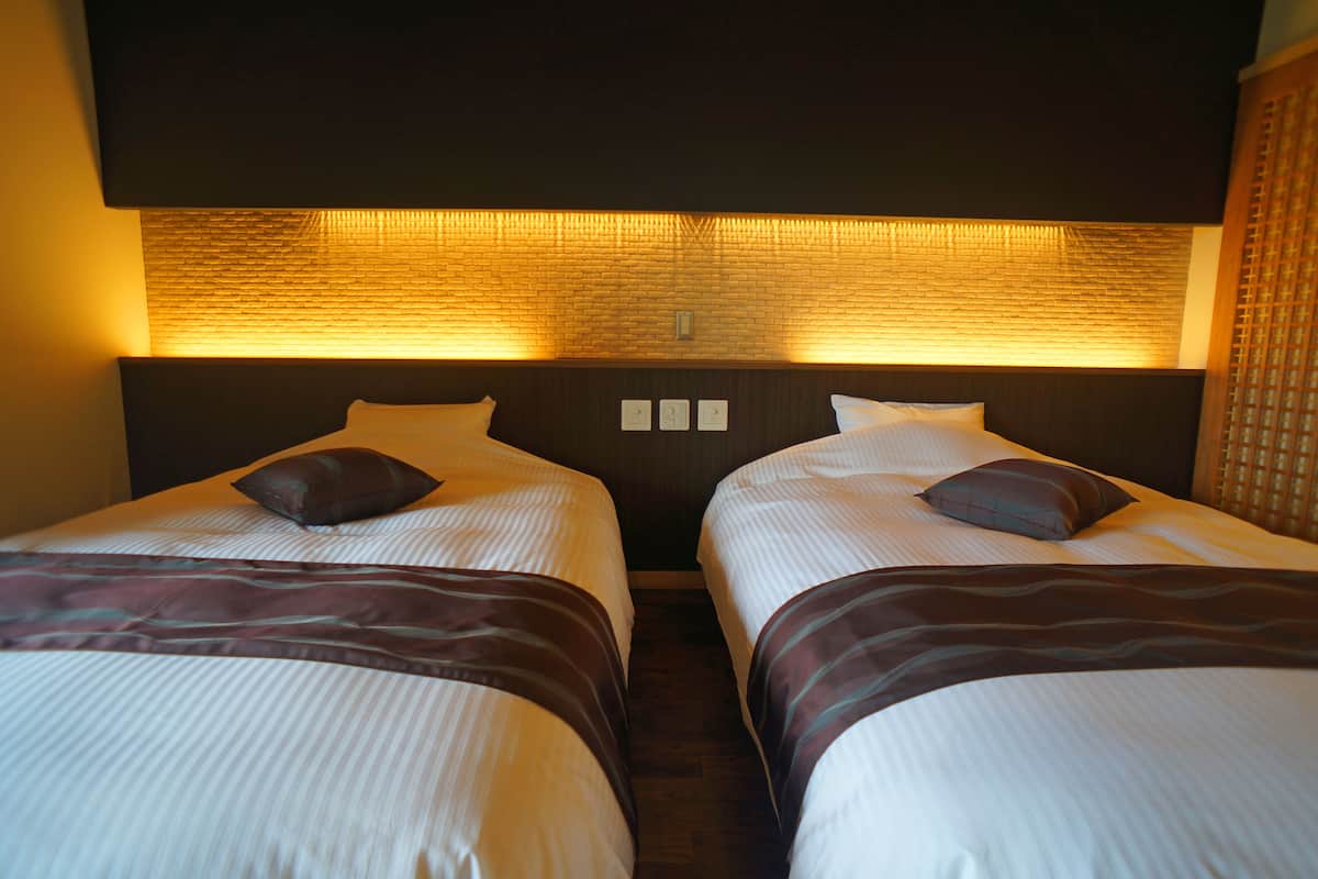 A hotel room with two beds, each with a pillow and a blanket.