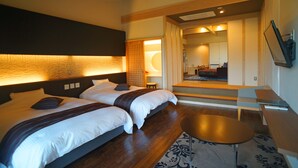 A hotel room with two beds, a sitting area with a table, and a view of the hotel's interior.
