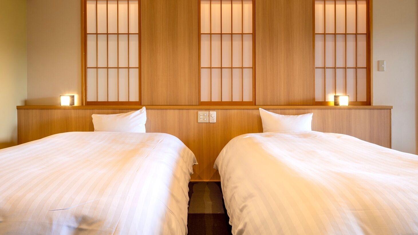 Habitación de hotel con dos camas, cabeceros de madera y una ventana tradicional al estilo japonés con puertas correderas.