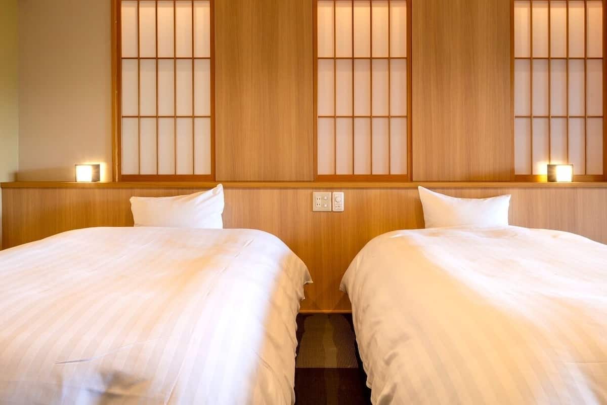 A hotel room with two beds, wooden headboards, and a traditional Japanese-style window with sliding doors.