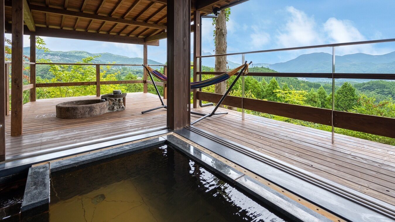 Una terraza de madera con un jacuzzi, una hamaca y vistas a un paisaje montañoso.
