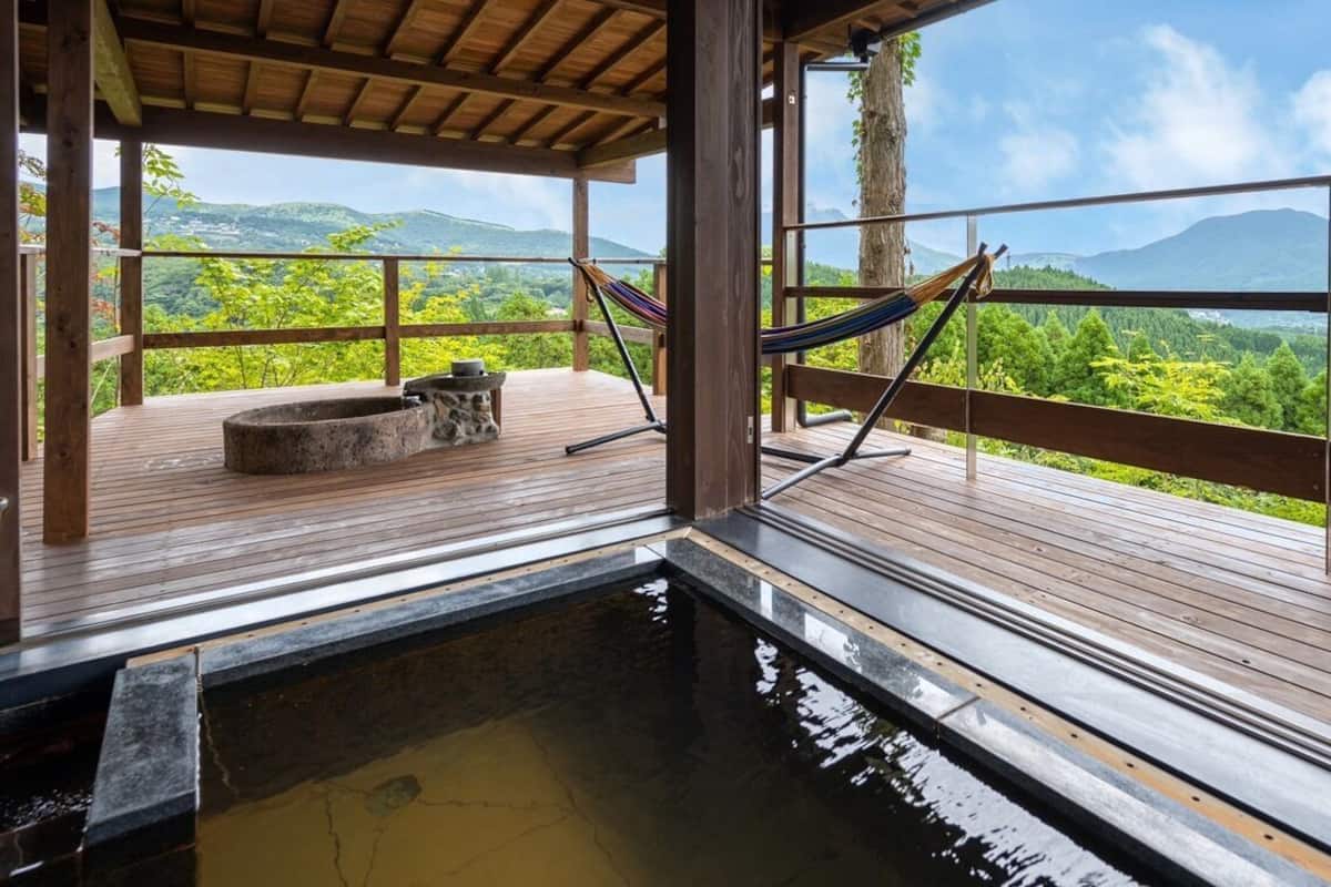 A wooden deck with a hot tub, a hammock, and a view of a mountainous landscape.