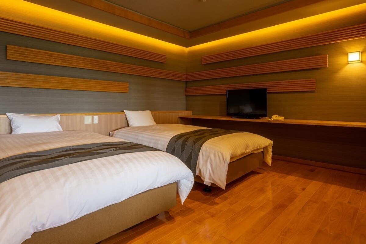 A hotel room with two beds, a flat-screen TV, and built-in wooden paneling on the walls.