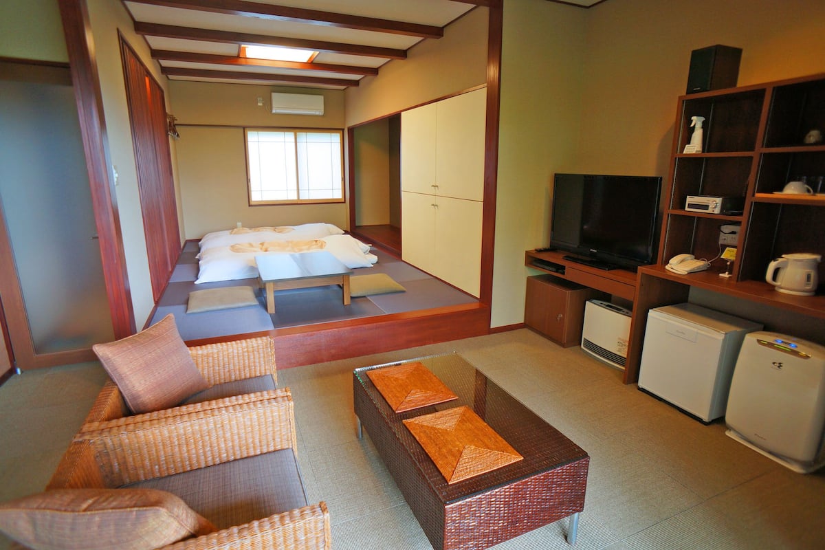 A traditional Japanese-style room with tatami flooring, a futon bed, a television, a refrigerator, and a small cabinet.