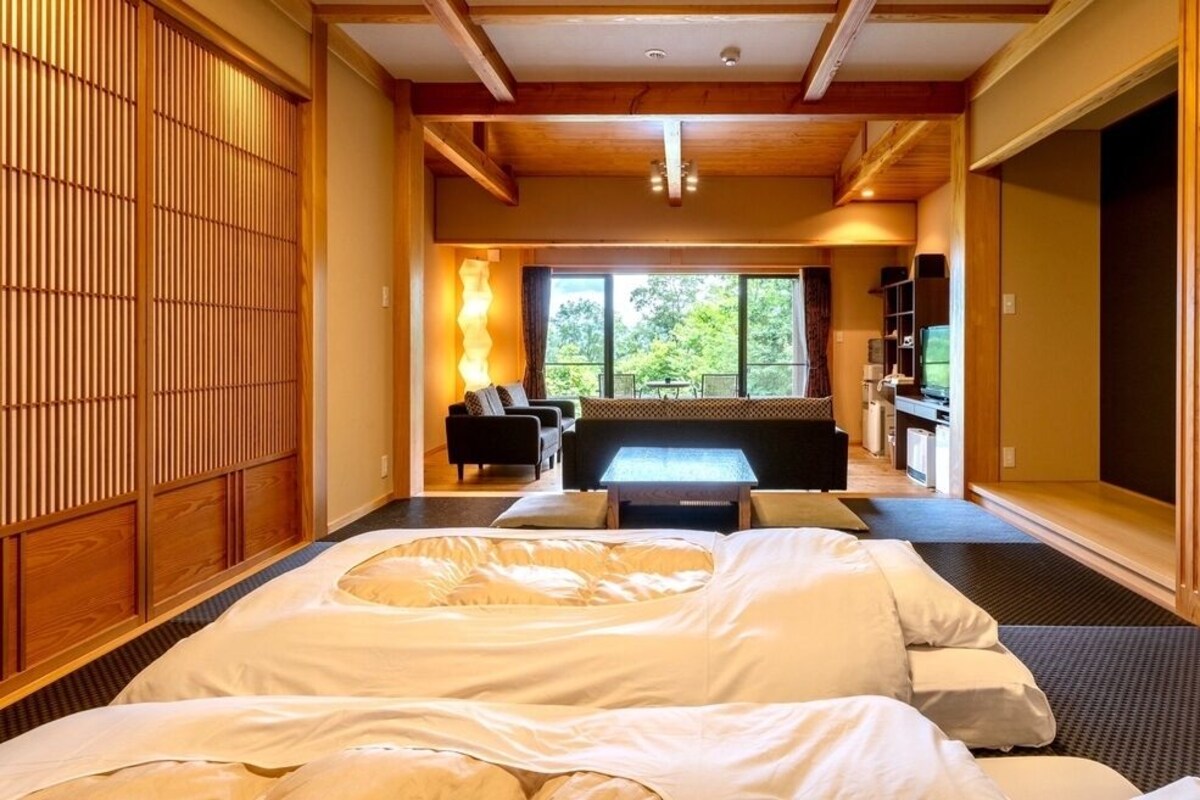 A room with a bed, a sofa, a massage table, and a view of the outdoors.