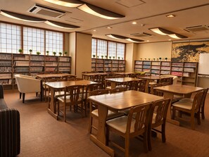A library with wooden tables and chairs, bookshelves, and decorative plants.