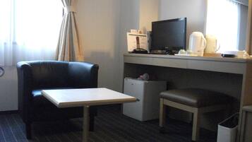 A hotel room with a black leather chair, a small table, a desk with a computer and a coffee maker, and a trash bin.