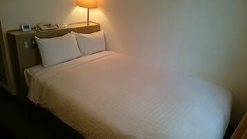 Een hotelkamer met een bed, een nachtkastje met een lamp, een telefoon en een wekker.