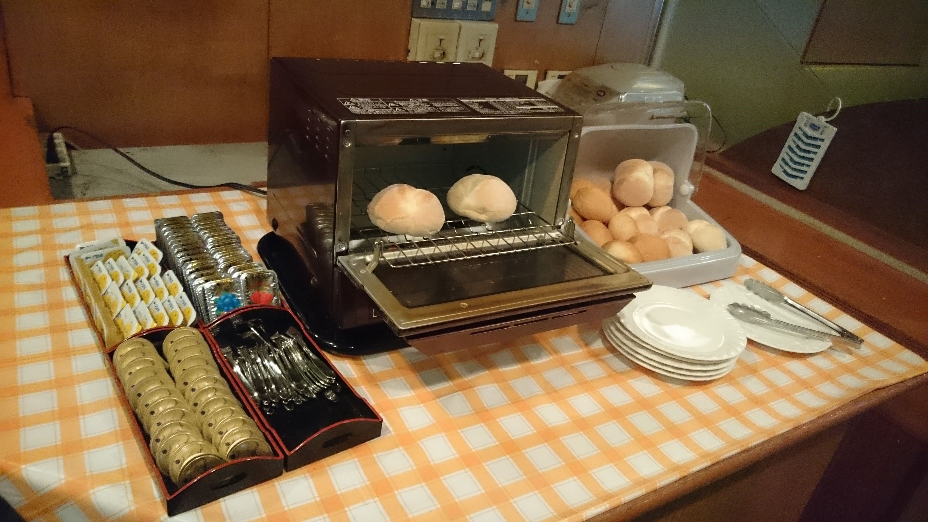 A buffet setup with a bread machine, a container of bread rolls, and a tray of sliced bread.