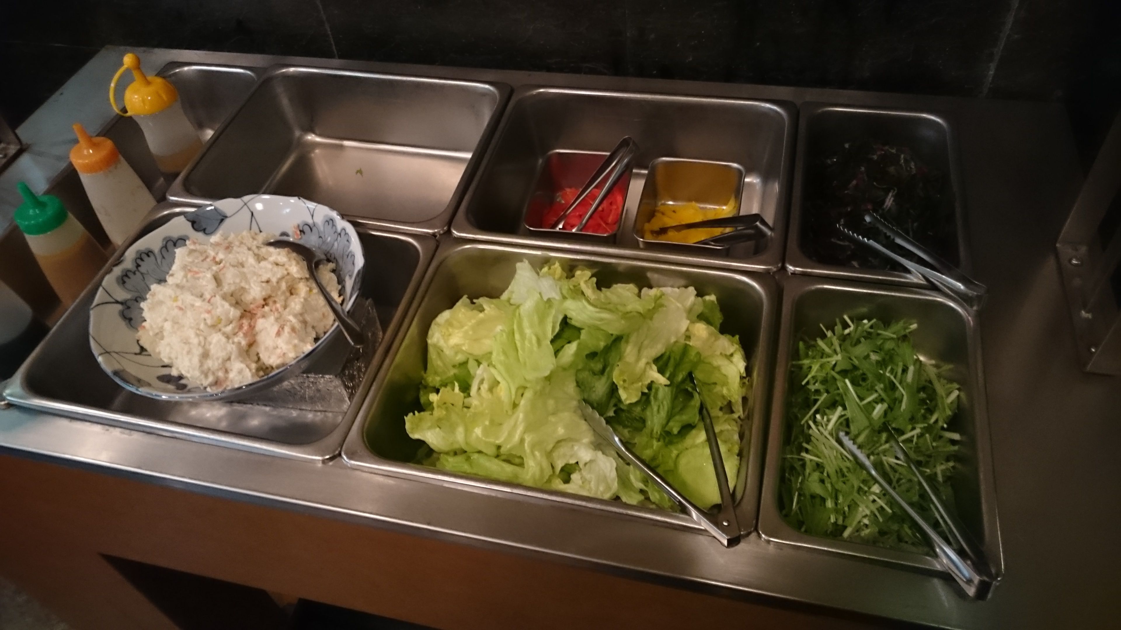 Un bufé con diversos alimentos, incluyendo un tazón de ensalada, verduras frescas y salsas.