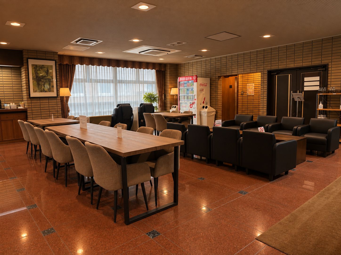 Une salle de conférence d’hôtel avec une longue table, de nombreuses chaises, un réfrigérateur rempli de Coca-Cola et un coin salon avec des canapés.
