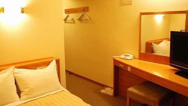 A hotel room with a bed, a desk with a telephone, a chair, and a television. - Hotel Crest Dio (Ibaraki)