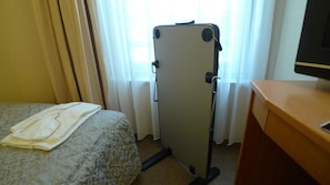 Ett hotellrum med en säng, ett skrivbord, en stol, en resväska och ett fönster med gardiner.