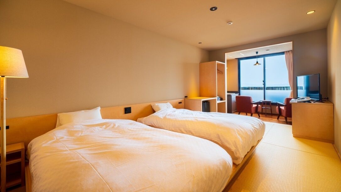 Ein Hotelzimmer mit zwei Betten, einem Schreibtisch, einem Sessel, einem Fernseher und einem Balkon mit Blick.