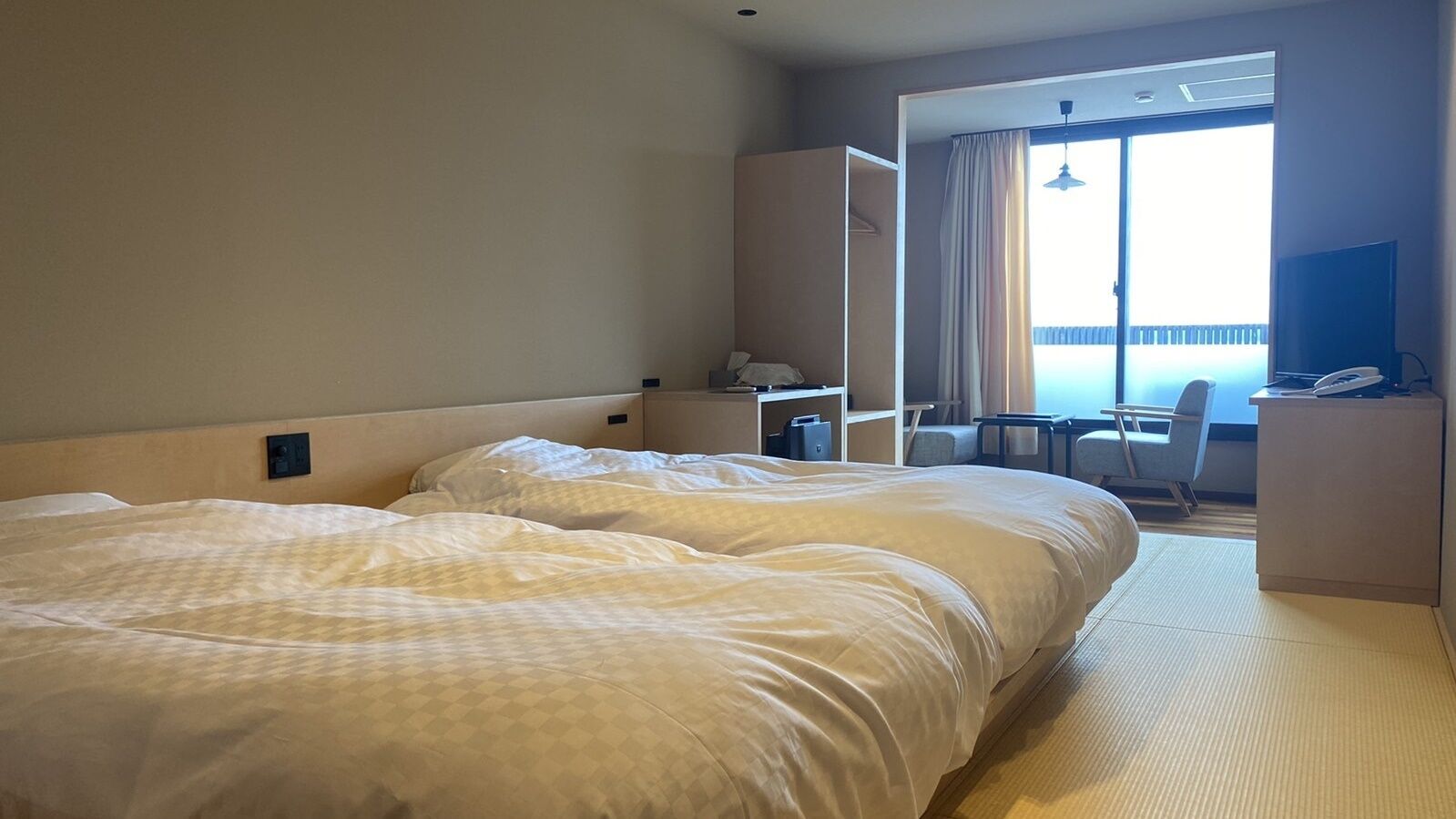 Ein Hotelzimmer mit zwei Betten, einem Schreibtisch, einem Stuhl und Blick ins Freie.