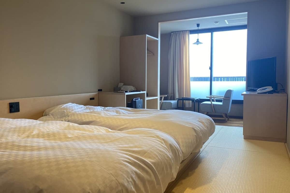 Habitación de hotel con dos camas, un escritorio, una silla y vistas al exterior.