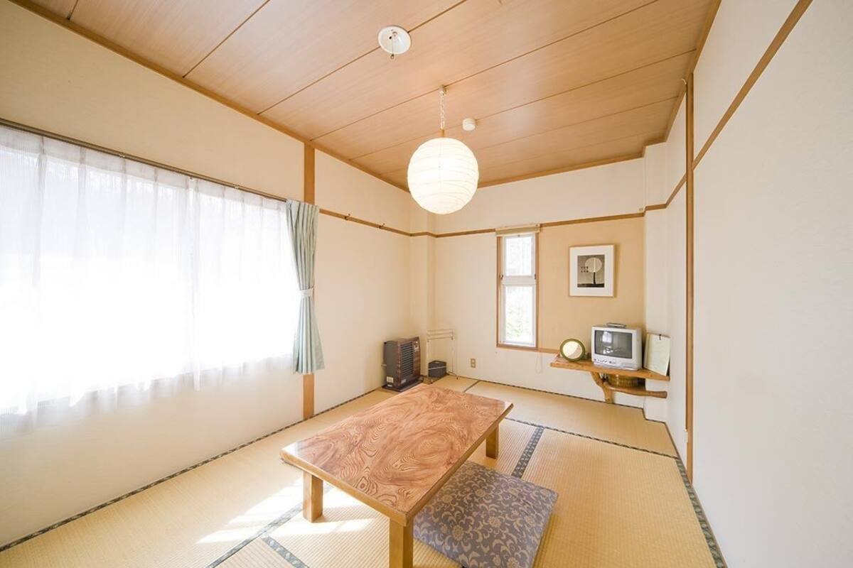 Habitació japonesa tradicional amb fons de tatami, una taula de fusta baixa, un fanal de paper penjant i un televisor sobre una estant.