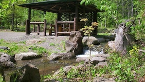 A rustic wooden pavilion with a lattice roof, surrounded by a natural setting with a small waterfall and rocks. - Alpine Inn Mizushiro (Matsumoto)
