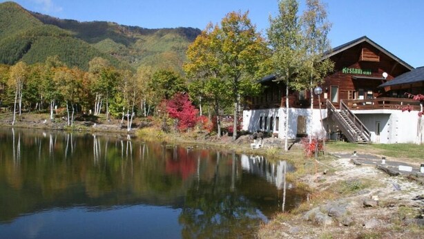 A rustic lodge with a wooden exterior, a dining area, and a view of a lake and mountains. - Alpine Inn Mizushiro (Matsumoto)