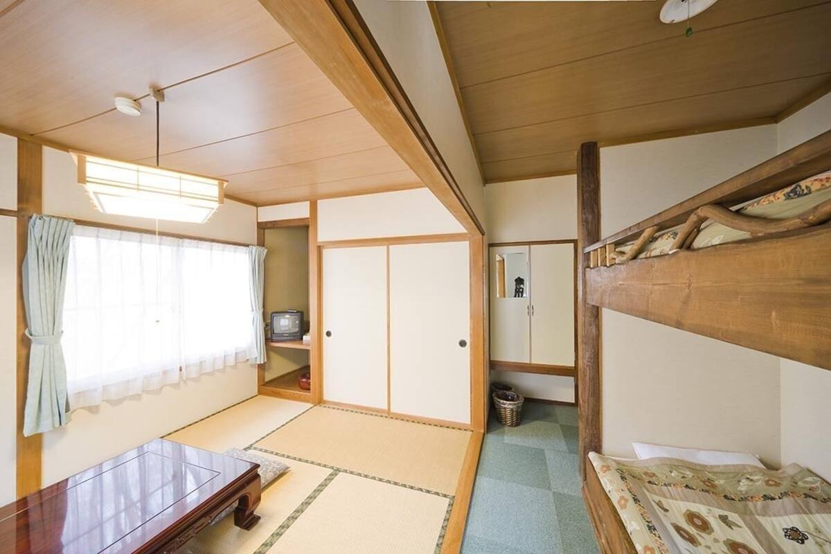 Una habitació japonesa tradicional amb fons de tatami, un llit de fusta baix, un escriptori i una porta corredissa.