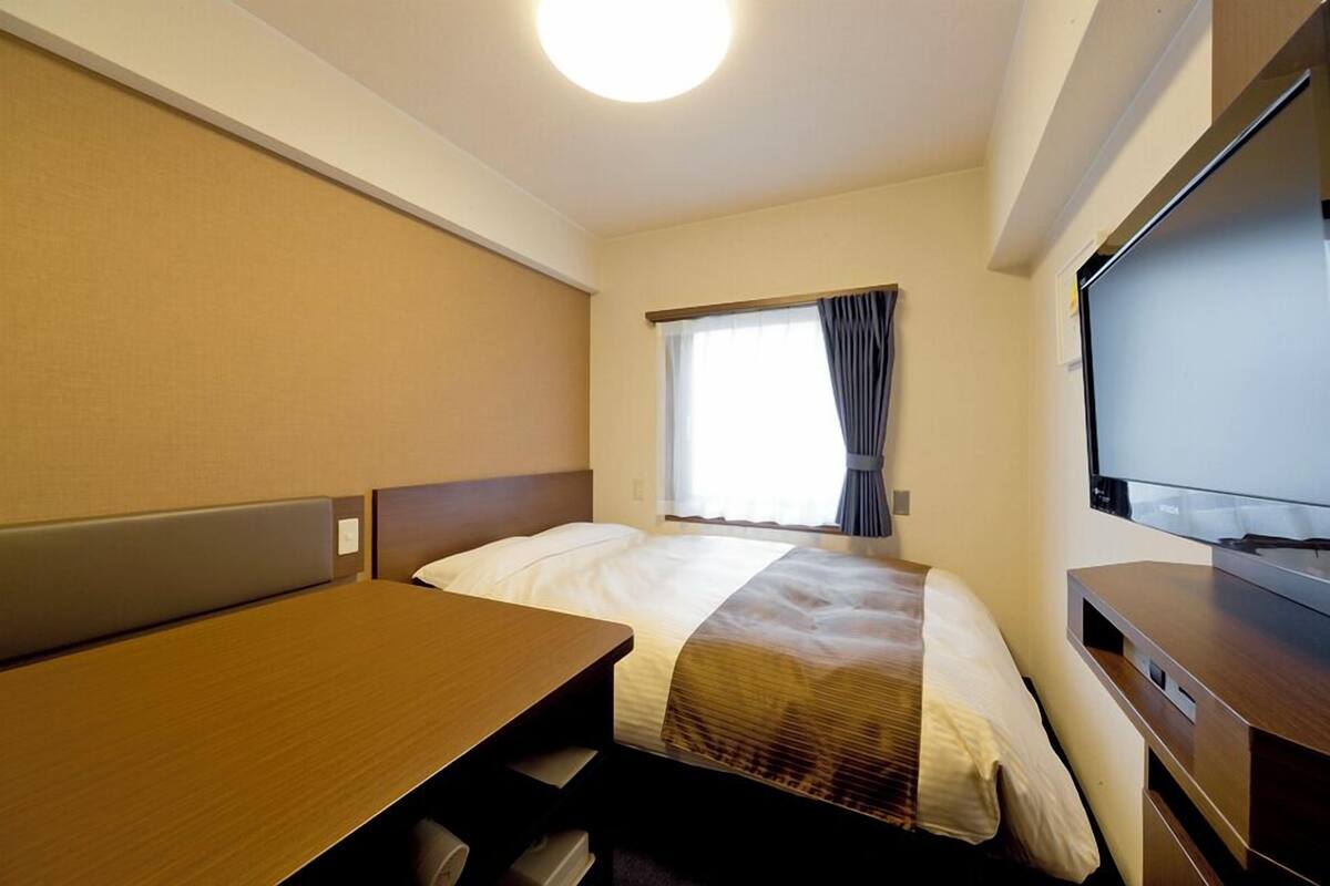 A hotel room with a bed, a desk, a television, and a window with curtains.