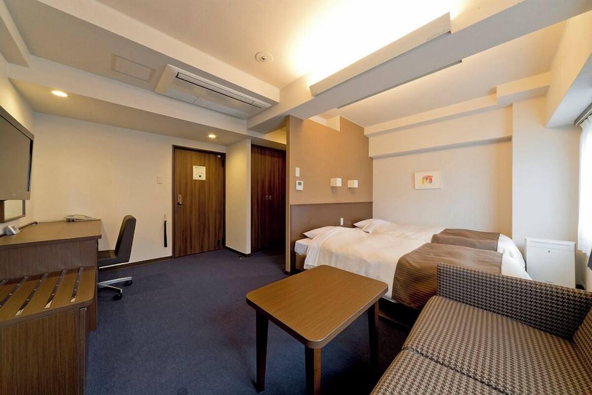 A hotel room with a desk, two beds, a sofa, and a small table.