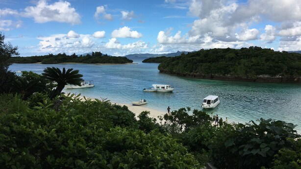A coastal landscape with boats on calm waters, surrounded by lush greenery and distant mountains. - Yugafu Kabira Ishigaki (Ishigaki)