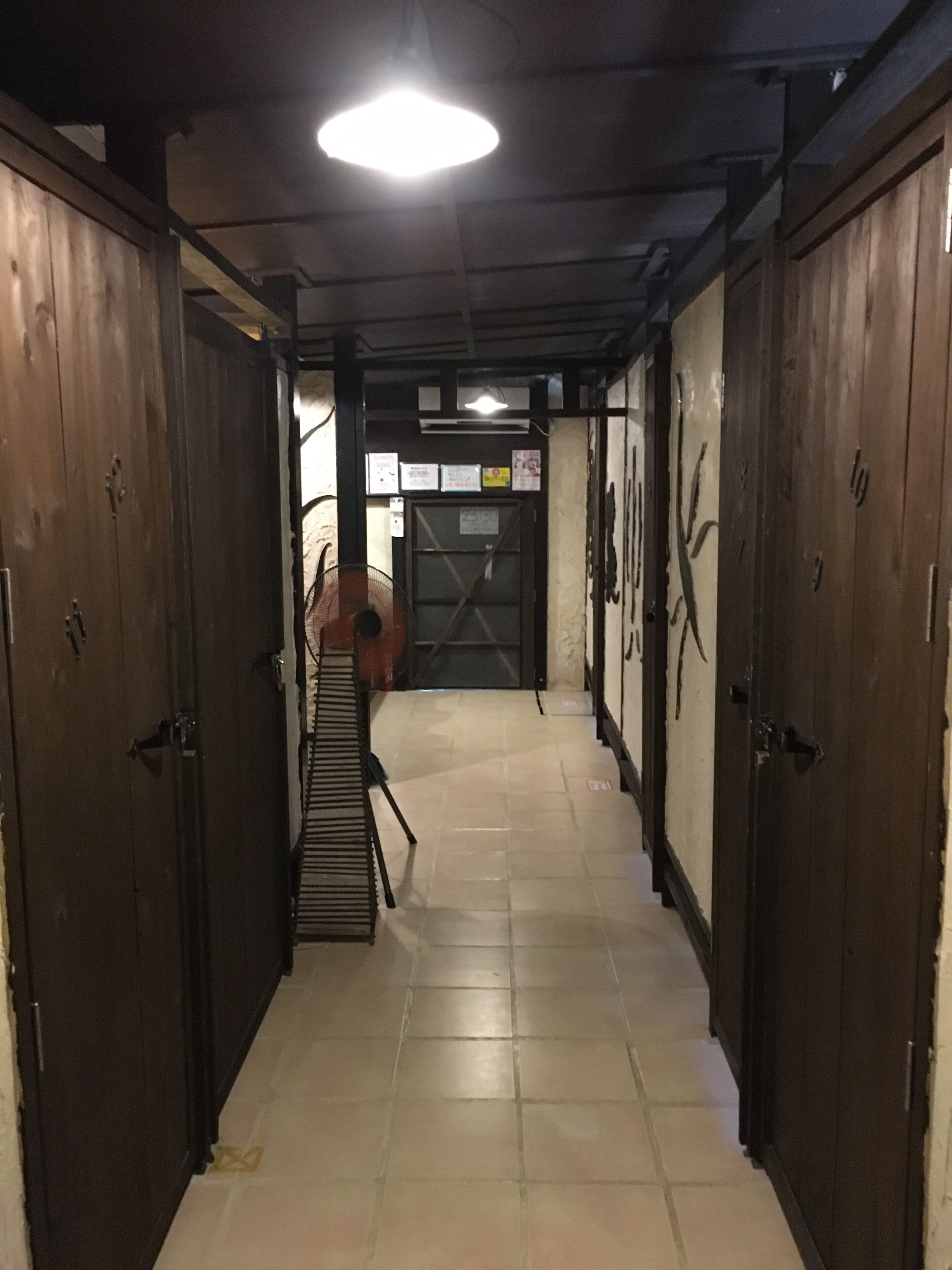 Un pasillo con puertas de madera, suelo de baldosas y una escalera que lleva a otra zona.