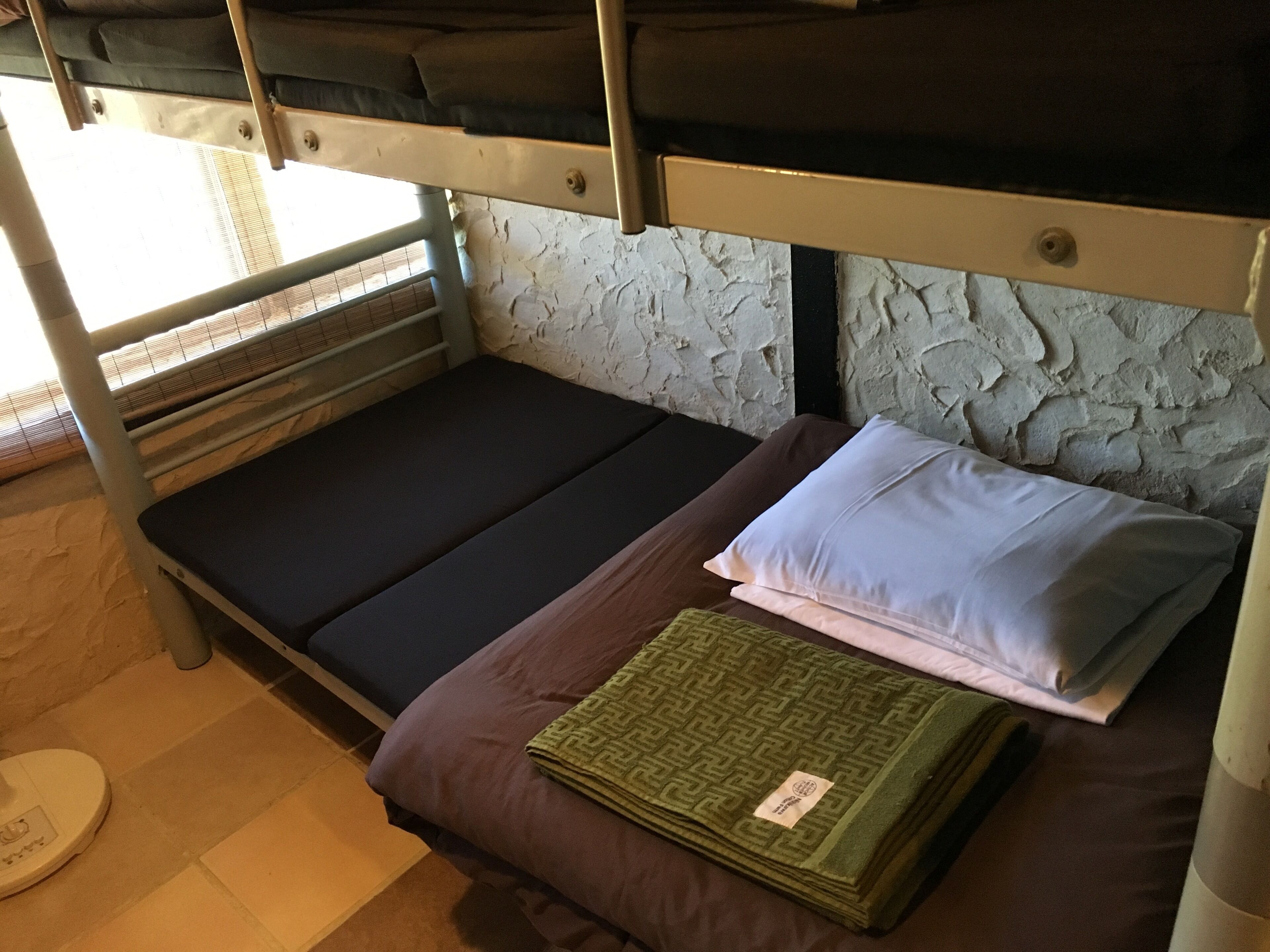 Un lit superposé avec un matelas, des oreillers et une couverture pliée.