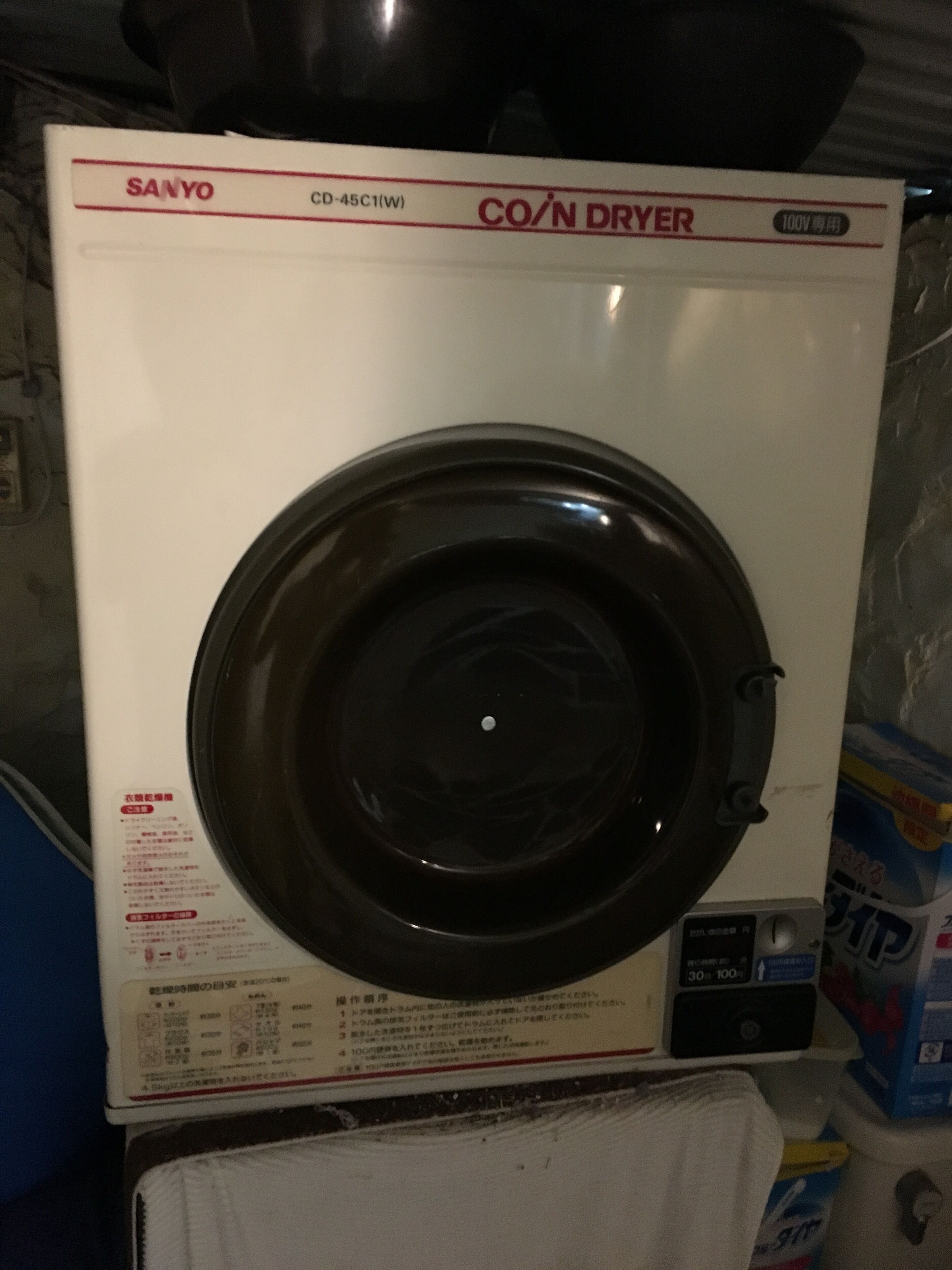 A white Sanyo CD-45C1(W) coin dryer with a black drum, control panel, and instruction manual.