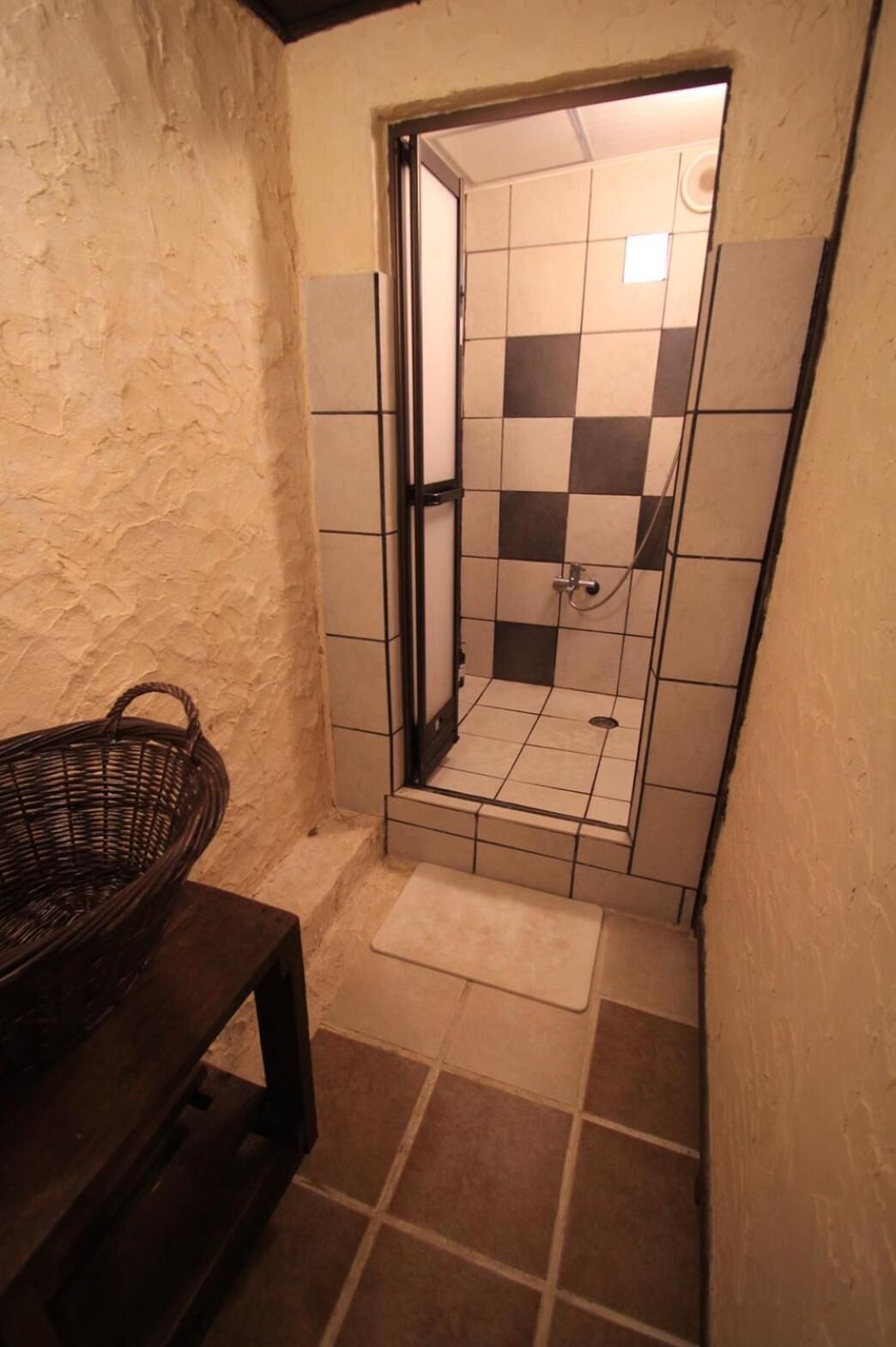 Une petite salle de bain avec un mur de douche à carreaux, un banc en bois et un sol carrelé.