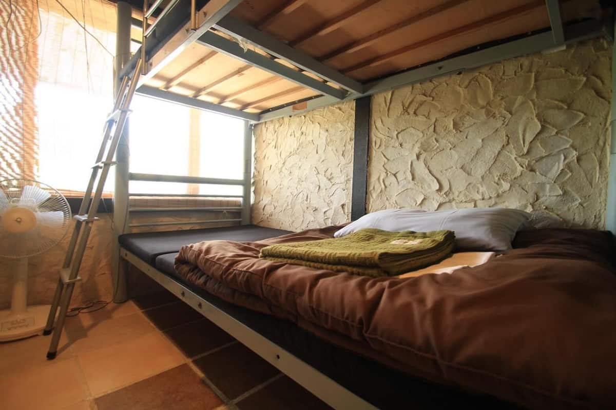 A bunk bed with a stone wall headboard, a window with a view, and a ladder.