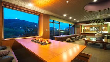 A modern interior with a large dining table, seating, and a view of a mountainous landscape.